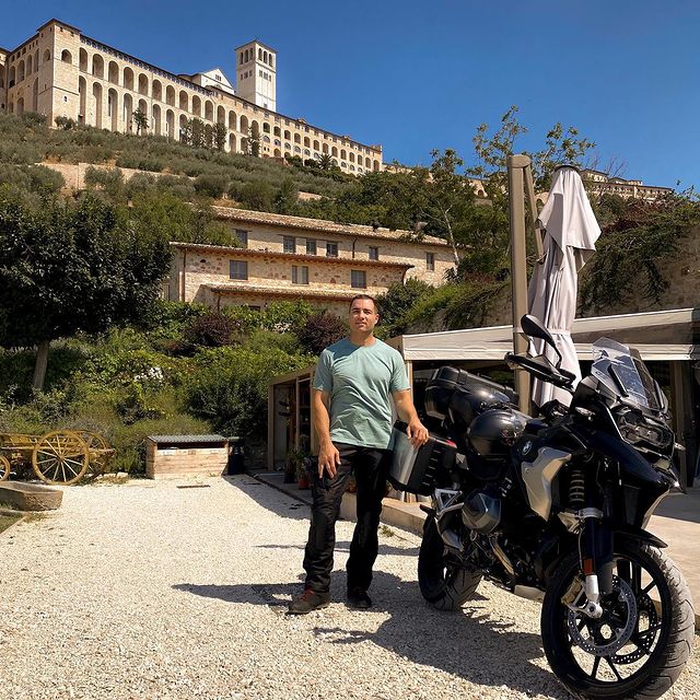 Chris Paciello in a blue t-shirt and black pants behind his black stylish motorbike.